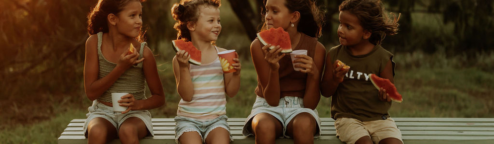 4 Children sit at a picnic table eating watermelon