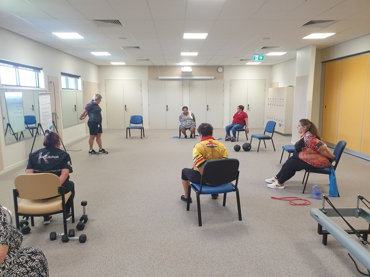 Members of the Women's group particpate in an exercise session in the gym activity room, led by a physiotherapist as an instructor
