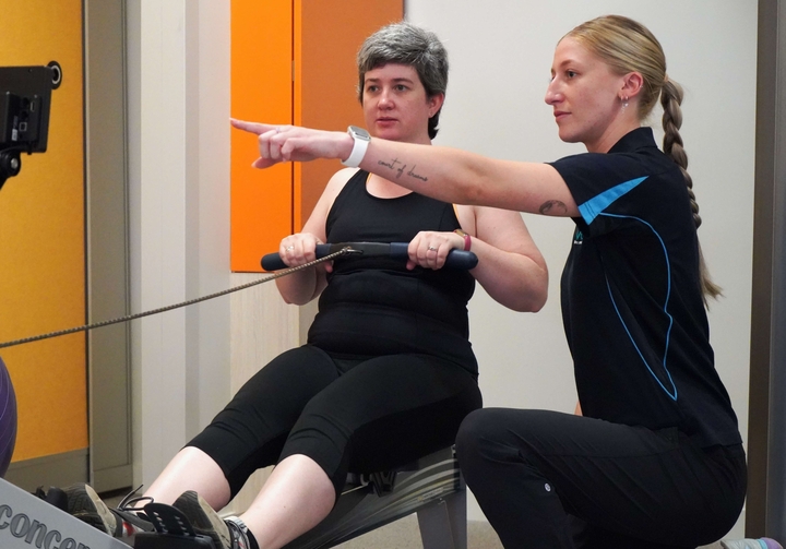 exercise physiologist explains rowing machine to patient