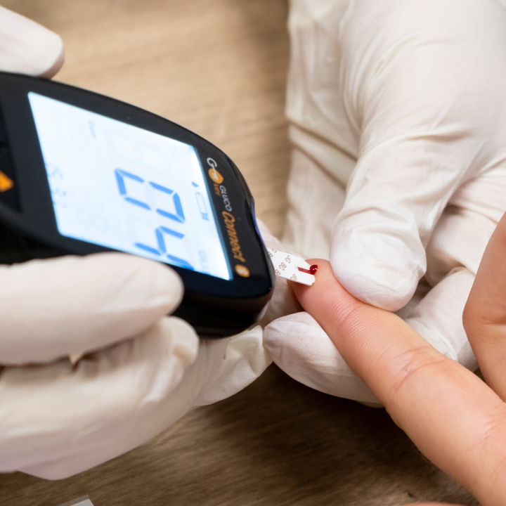 Gloved hand holds blood gluclose monitor to blood drop on patients finger