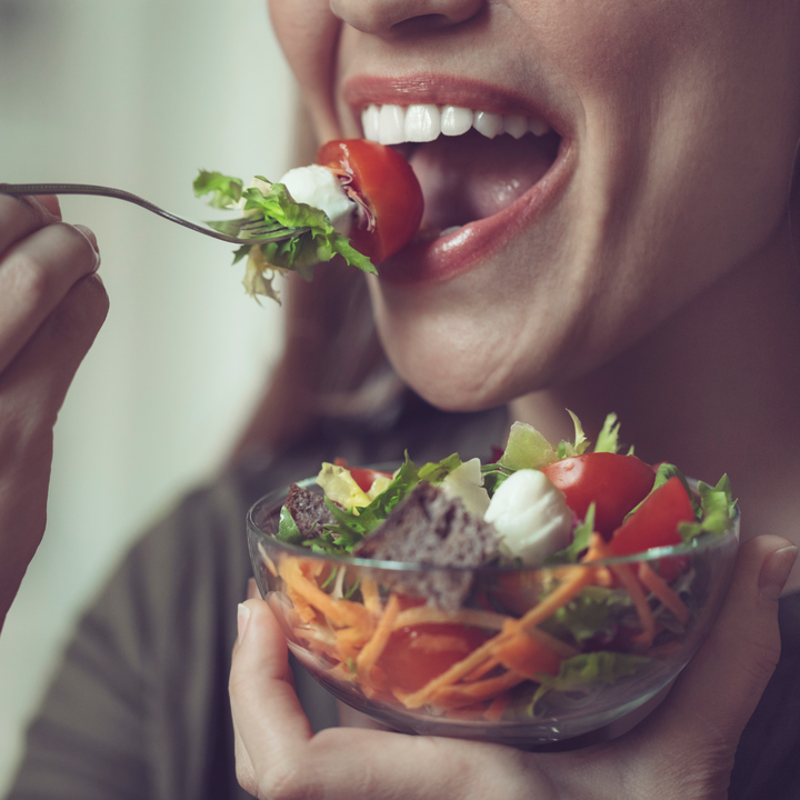 Woman holding bowl of salad and lifting forkful of food to open mouth