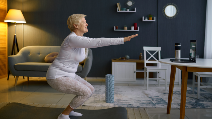 Older woman performs squat from instructional video