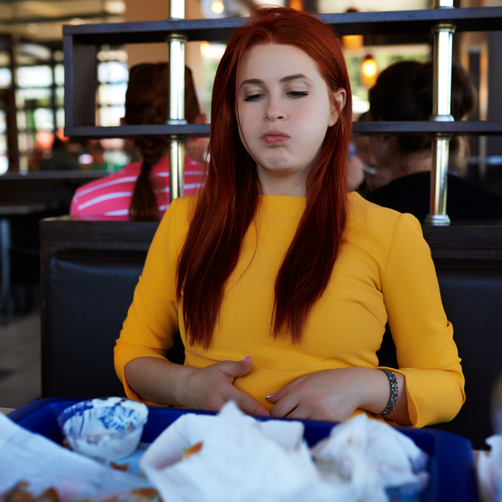 Woman sits in front of finished meal looking uncomfortable