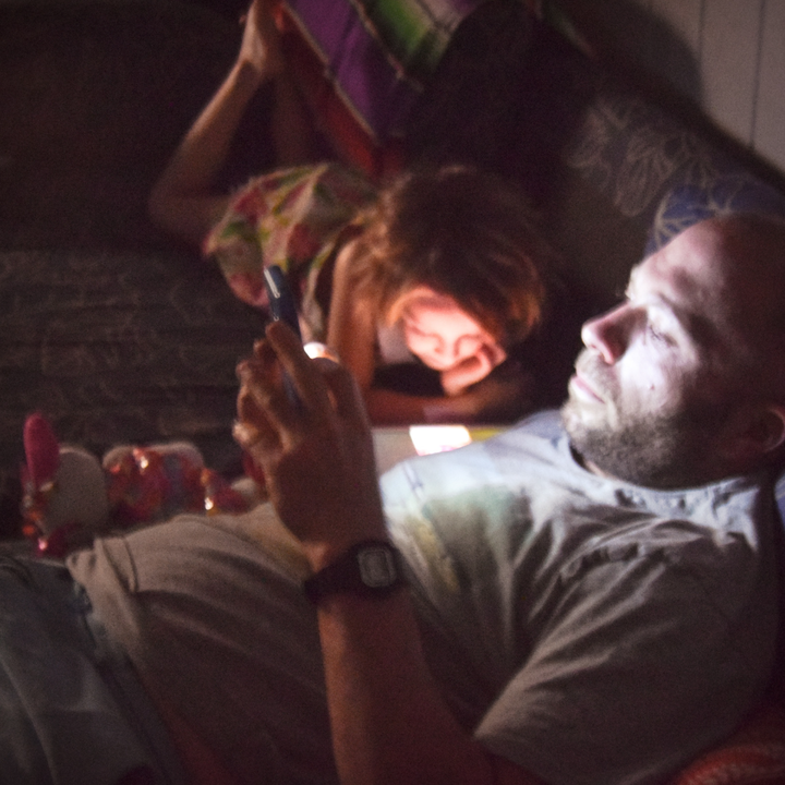 father and daughter sit in dark watching screens