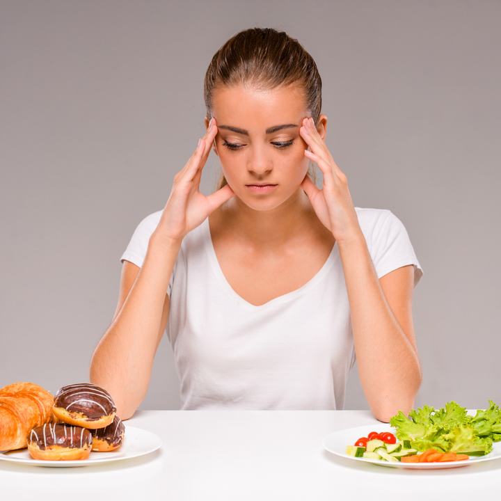 Woman sits and contemplates a plate of donuts vs. a plate of salad