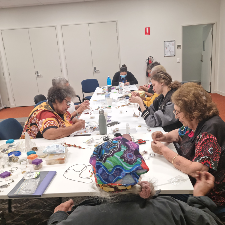 Members of the Women's group gathered around a table participating in jewellery beading.