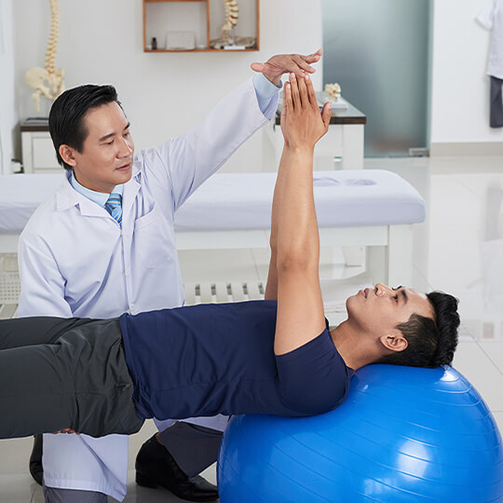 Physio helps rehabilitate young man on large exercise ball