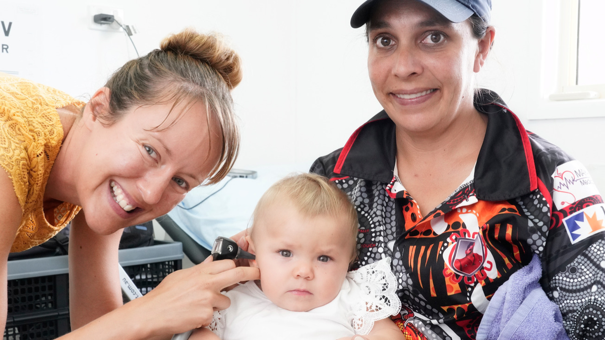 Mother holds infant in her lap while audiologist checks infants ears.