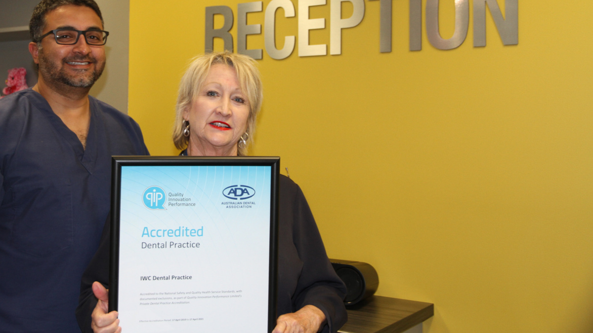 Dentist and Dental Assistant stand in Dental Reception holding accreditation certificate