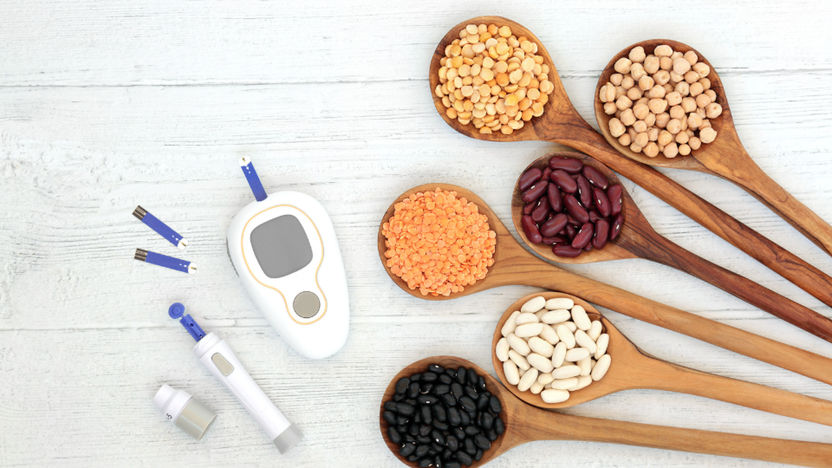wooden spoons holding healthy grains and beans sitting beside blood glucose monitoring machine