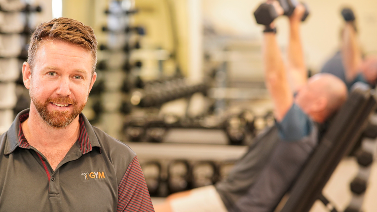Exercise Physiologist looks at camera while man works out in gym