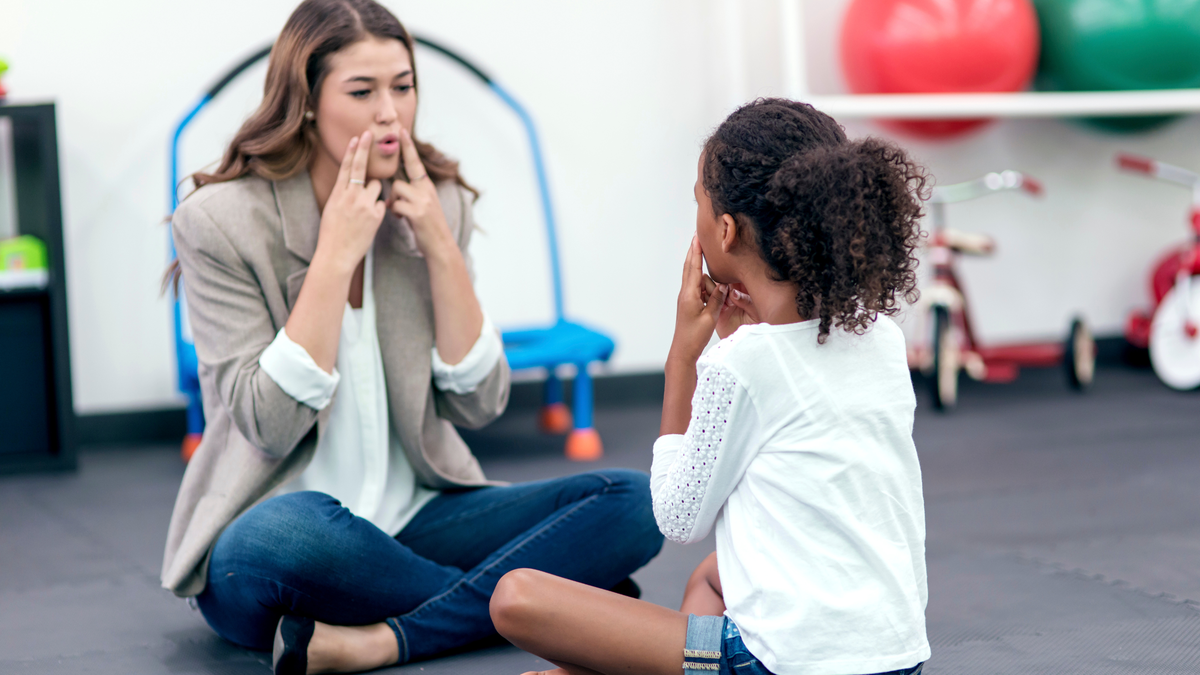 speech therapist uses fingers on face to teach child a sound
