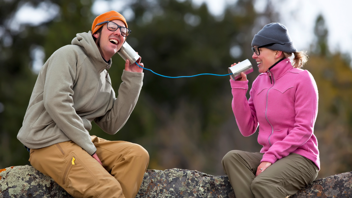 man and woman sit on a log with a can and string telephone