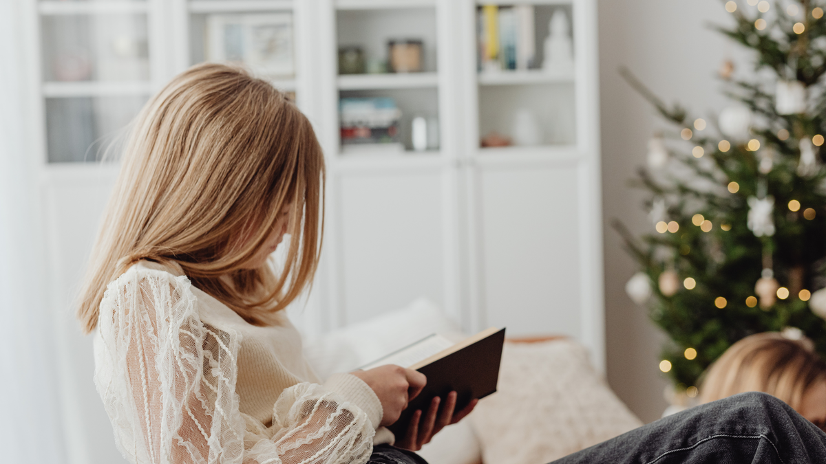 woman reads book by a christmas tree